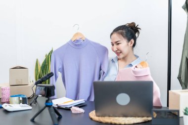 Moda tasarımcısı kadın tasarımcısı ürünleri satmak ve çevrimiçi sipariş almak için canlı yayın videosu yayınlıyor ve evdeki müşteriye teslimat için giysileri paketleyip kutulara koyuyor..