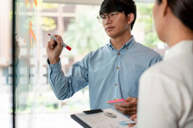 İki işletme yöneticisi, ofiste birlikte pazarlama planının planlanmasına yönelik yeni bir iş projesi hakkında fikir alışverişinde bulunmak için kilit noktayı duvara yazıp not alıyorlar..