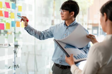 İki işletme yöneticisi, ofiste birlikte pazarlama planının planlanmasına yönelik yeni bir iş projesi hakkında fikir alışverişinde bulunmak için kilit noktayı duvara yazıp not alıyorlar..