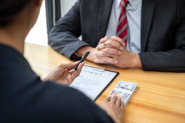 Rüşvet veren işadamına bir kalem veriyor ve iş adamına arazi ve gayrimenkul satın almada yolsuzluk yaparken sözleşme imzalaması için şartları sunuyor.