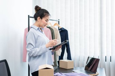 Moda tasarımcısı kadın tasarımcısı ürünleri satmak ve çevrimiçi sipariş almak için canlı yayın videosu yayınlıyor ve evdeki müşteriye teslimat için giysileri paketleyip kutulara koyuyor..