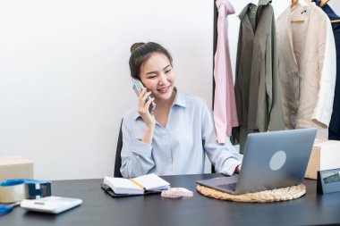 Moda tasarımcısı kadın ürünleri satar ve müşteriden sipariş alır ve müşteriye eve teslimat için kıyafet paketlerini kutulara doldurur..