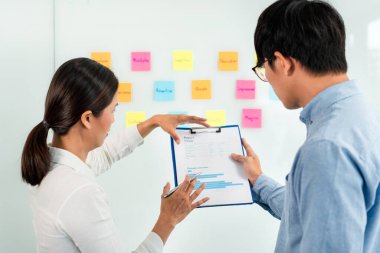 İki işletme yöneticisi, ofiste birlikte pazarlama planının planlanmasına yönelik yeni bir iş projesi hakkında fikir alışverişinde bulunmak için kilit noktayı duvara yazıp not alıyorlar..