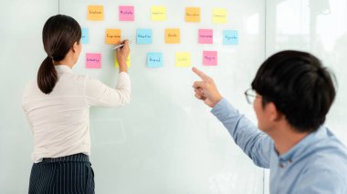 İki işletme yöneticisi, ofiste birlikte pazarlama planının planlanmasına yönelik yeni bir iş projesi hakkında fikir alışverişinde bulunmak için kilit noktayı duvara yazıp not alıyorlar..