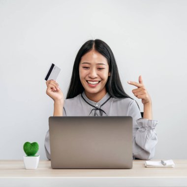 Asyalı kadın kredi kartı tutuyor ve internet üzerinden ürün satın almak için dizüstü bilgisayar kullanırken, kredi kartını da evde internet bankacılığına para ödemek için kullanıyor.