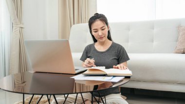 Müşteriden sipariş almak için dizüstü bilgisayar kullanan Asyalı serbest kadın ve çevrimiçi pazarlama teslimatı sırasında ürünleri kontrol ederken ev ofisteki defterde müşteri bilgileri yazıyor.