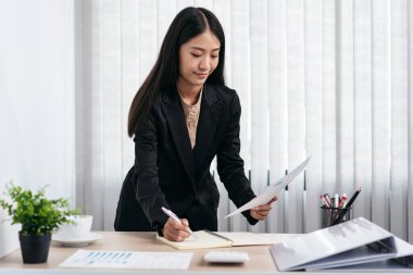 İş kadını elinde mali tabloları okumak için iş belgesi tutuyor ve ofiste yeni iş yatırımlarının analizi sırasında deftere notlar alıyor.