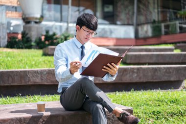 Genç işadamı, elinde belge ve iş projesiyle dışarıda otururken mali raporları kontrol ediyor.