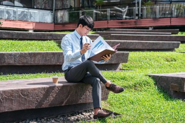 Genç işadamı, elinde belge ve iş projesiyle dışarıda otururken mali raporları kontrol ediyor.