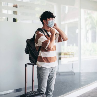 Tıbbi maske takan turist arkadaşlarıyla akıllı telefondan konuşurken, tatilde bavullarıyla birlikte Cvid-19 salgını sırasında normal bir yaşam tarzı sürüyorlar.