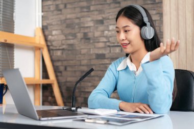 Kadın öğretmen kulaklık takıyor, dizüstü bilgisayar kullanıyor ve her ne kadar kamera ile webcam 'de video konferansında yeni dersler verirken matematik denklemlerini ve öğrencilere e-öğrenim kursunda fizik dersi veriyor olsa da