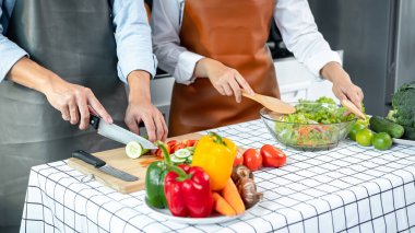 Asyalı romantik çift, salatalık ve domatesli ve bıçaklı salatayı doğruyor ve kasede sebze salatasını karıştırırken evde birlikte sağlıklı yemek pişiriyorlar.