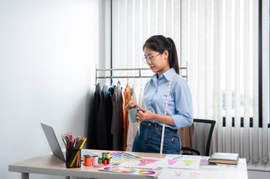 Çalışan ve düşünen kadın moda tasarımcısı atölyede yeni kıyafet koleksiyonu ürünü yapmak için renk örnekleri ve kumaş seçmeye karar verdi.