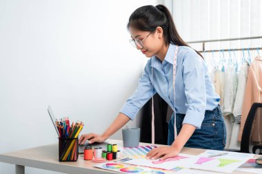 Çalışan ve düşünen kadın moda tasarımcısı atölyede yeni kıyafet koleksiyonu ürünü yapmak için renk örnekleri ve kumaş seçmeye karar verdi.