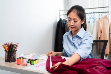 Kadın moda tasarımcısı çalışıyor ve kumaş malzemelerini ölçüyor. Yeni kıyafet koleksiyonu ürünleri yapmak için renk örnekleri seçiyor..