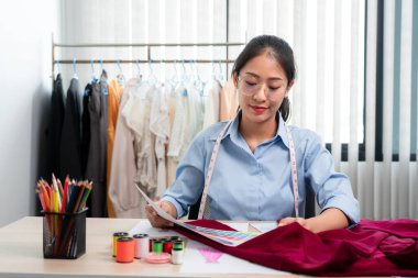 Kadın moda tasarımcısı çalışıyor ve kumaş malzemelerini ölçüyor. Yeni kıyafet koleksiyonu ürünleri yapmak için renk örnekleri seçiyor..