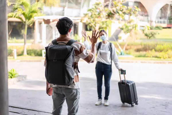Two asian tourist to saying goodbye when comeback from vacation trip together while holding luggage and wearing medical face mask to protection from coronavirus for travel with new normal lifestyle