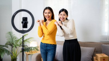 İki kadın fotoğraf makinesiyle poz veriyor. İkisi de gülümsüyor ve eğleniyor gibi görünüyorlar.