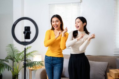 İki kadın dans ediyor ve biri cep telefonu tutuyor. Sahne eğlenceli ve neşeli.