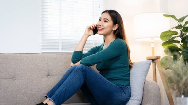Bir kadın kanepede oturuyor ve cep telefonuyla konuşuyor. Gülümsüyor ve sohbetten zevk alıyor.