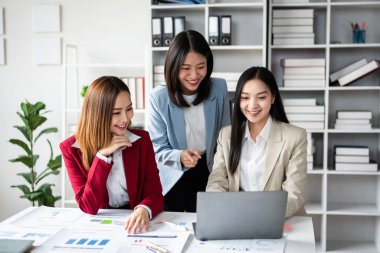 Three women are sitting at a desk with a laptop open. They are smiling and seem to be having a good time clipart