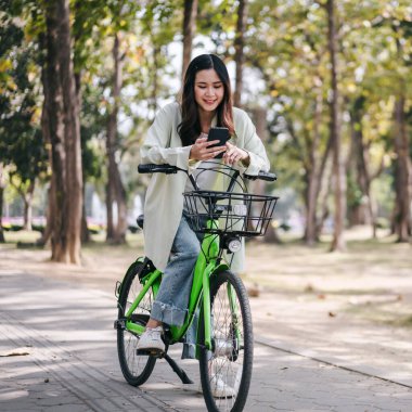 Yeşil bir bisiklete binen bir kadın telefonuna bakıyor. Sahne rahat ve rahattır, çünkü kadın arabasının keyfini çıkarıyor ve telefonunu kontrol ediyor.