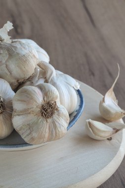 Tahta kesme tahtasının üzerinde bir kase taze organik sarımsak soğanı, karanfil ve sarımsak ezici. Seçici odak. 