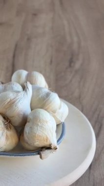 Tahta kesme tahtasının üzerinde dönen bir kase taze organik sarımsak soğanı ve karanfil. Seçici odak. 