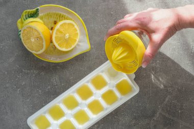 Yarım limon, plastik narenciye sıkacağı ve beyaz buz kalıbına taze limon suyu döken bir kadın eli. Ev yapımı limonlu buz..