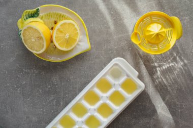 Yarım limon, plastik narenciye suyu, taze limon suyuyla birlikte beyaz bir buz küpü. Ev yapımı limonlu buz küpleri için kompoziton