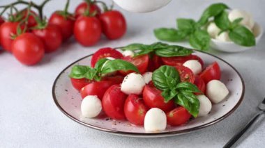 Making Italian caprese salad with sliced tomatoes, mozzarella, basil, olive oil on a light background. Pouring oil on salad. Italian food. Healthy salad. Summer food.
