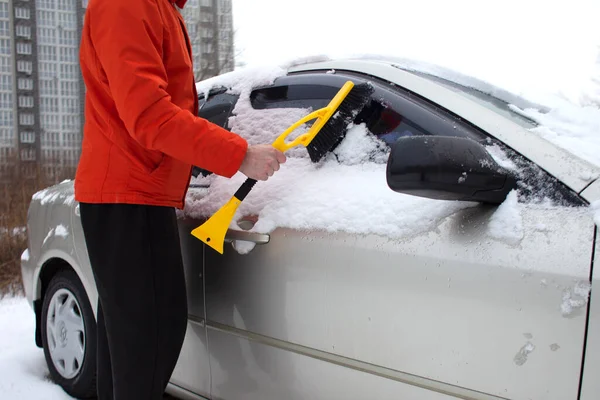 若い男は車のブラシで雪をきれいにし男は冬に車の世話をする — ストック写真