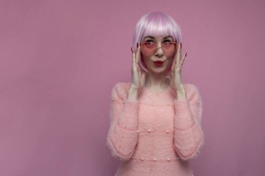 Gözlüklü pembe saçlı genç kız şaşırır ve pembe bir arka plana bakar.