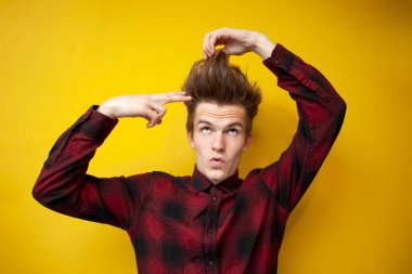 Tuhaf saç stili olan genç, sarı izole edilmiş arka planda kendini makasla kesiyor. Uzun saç problemi.