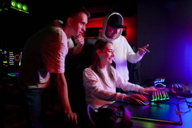 young guys gamers teach a girl to play a computer game look at the monitor and communicate, a company of young people in a computer club
