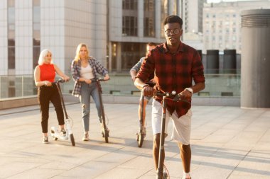 Şehirdeki arkadaşlarıyla birlikte elektrikli scooterlı Afro-Amerikalı bir adam. Irklar arası gençler ekolojik ulaşım kullanıyor.