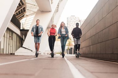 Irklar arası genç arkadaşlar şehirde elektrikli scooter kullanıyor, çok ırklı gençler elektrikli araç kullanıyor.