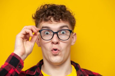 Gözlüklü genç kıvırcık adam kameraya bakar ve şaşırır, bir öğrenci gözlüklerini ayarlar, yakın plan.