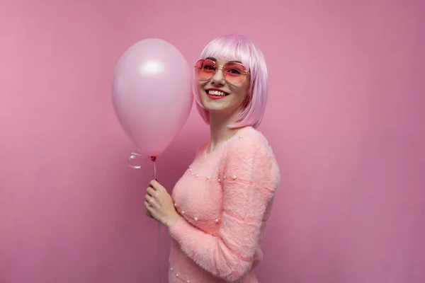 young girl with pink hair holds a pink balloon and smiles, hipster with colored hair