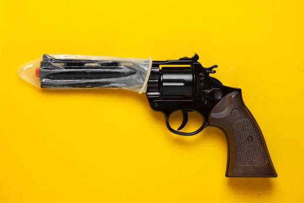 condom put on the barrel of a gun on a yellow background, the concept of a strong contraceptive, the concept of safe sex