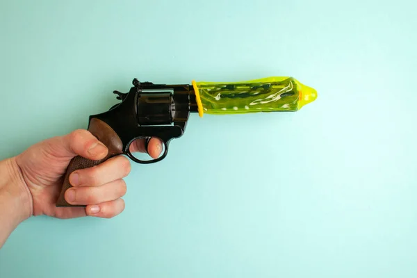 hand holds a gun dressed in a yellow condom on a blue background, the concept of erection and male sexual health, the concept of safe sex