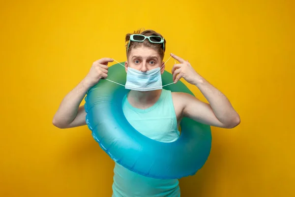 young guy in the summer on vacation with an inflatable swim ring wears a medical antiviral mask, the concept of the coronavirus epidemic