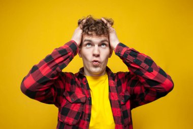 young surprised guy with curly hair holds his hair with his hands and looks up, the guy is doing the styling