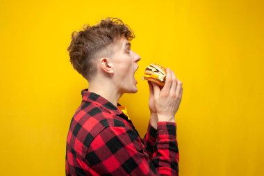 young curly guy student eats a burger on a yellow background, a man with fast food