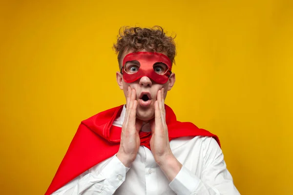 young shocked guy in superhero costume shows surprise on yellow background, shocked superman