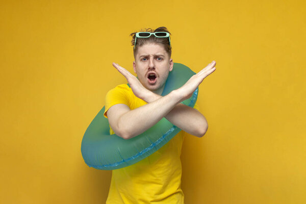 Молодой парень с надувным плавательным кольцом в отпуске летом не позволяет своими руками и показывает стоп, знак табу