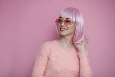 young girl with pink hair straightens her short hair and smiles on a pink background