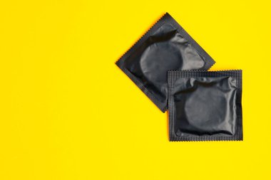 two black condom on yellow background, top view, safe sex concept