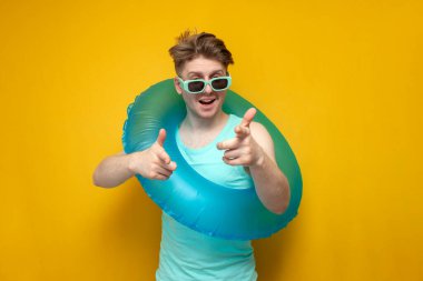 I choose you. a young guy with an inflatable swimming ring shows his hands to the camera on a yellow background, a man poses on vacation in the summer