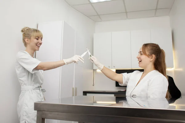 two female nurses in uniform fight with thermometers in the hospital, funny doctors fight and smile against the backdrop of the workplace